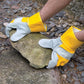 Person wearing yellow and gray gloves holding a stone on a rocky ground.