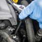 Person wearing blue gloves using a tool on car engine components.