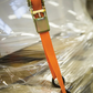 Orange ratchet strap with a gold buckle on a clear plastic sheet background