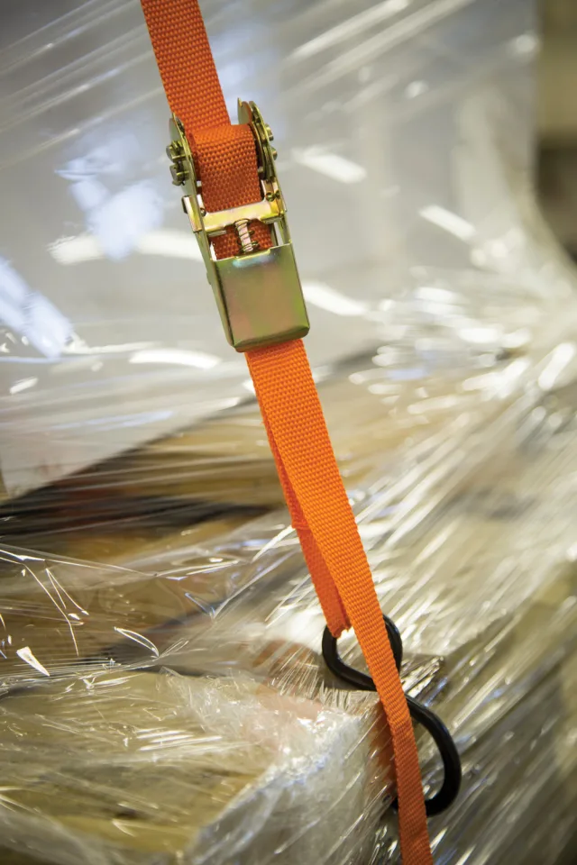 Orange ratchet strap with a gold buckle on a clear plastic sheet background