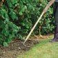 Person using a garden fork in a garden setting with green plants and grass.