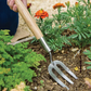 Person using a garden fork in a garden with plants and flowers.