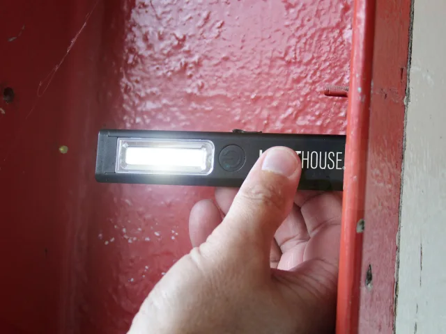 Hand holding a flashlight against a red door