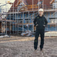 Person in construction gear standing on a construction site with scaffolding and building materials in the background.