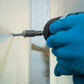 Hand using a drill with a screwdriver bit to tighten a screw into a wall.