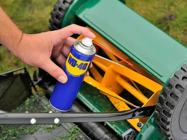 Person using WD-40 on a lawn mower