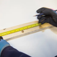 Person measuring a wooden board with a tape measure and marking it with a pencil.