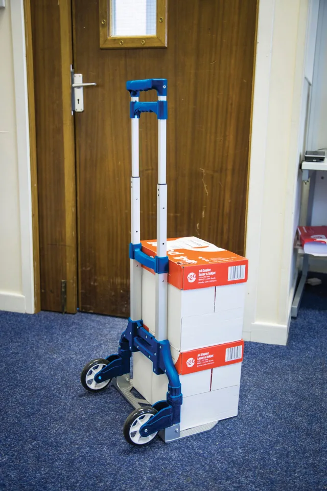 Blue and white dolly with stacked boxes against a wooden door.