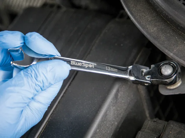 Person wearing blue gloves holding a BlueSpot wrench on a dark surface